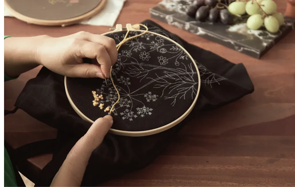 A woman learning embroidery basics by stitching yellow flower shapes on a black tote bag.