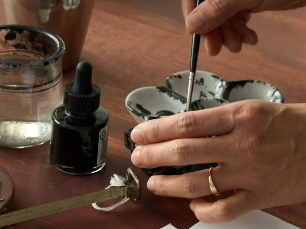 Author mixing ink with water on a flower-shaped ink palette using a brush.