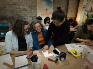 Teacher demonstrating how to ink a lino block and position printmaking paper.