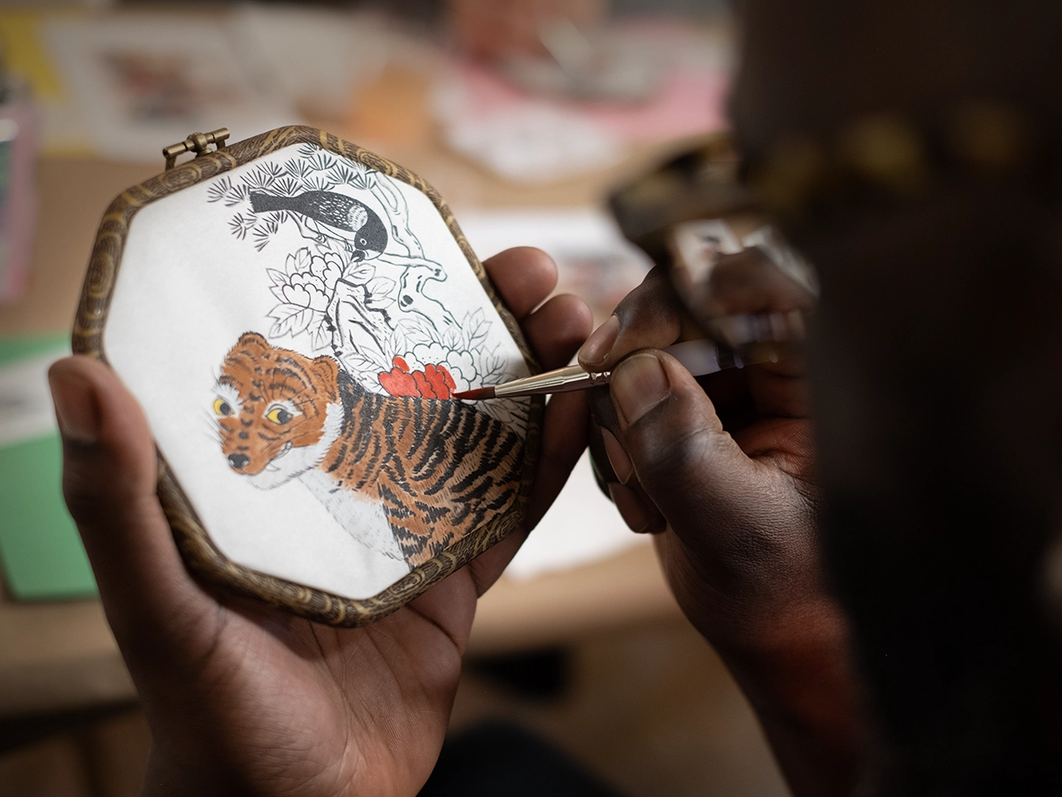 Man painting a tiger, magpie, and flowers in a traditional Korean Minhwa style.