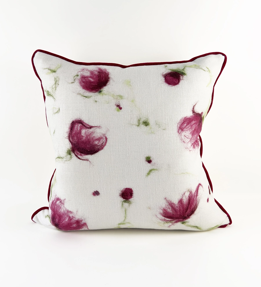 Square pillow with red piping and red floral shapes created using Astrid’s Paint with Wool technique.