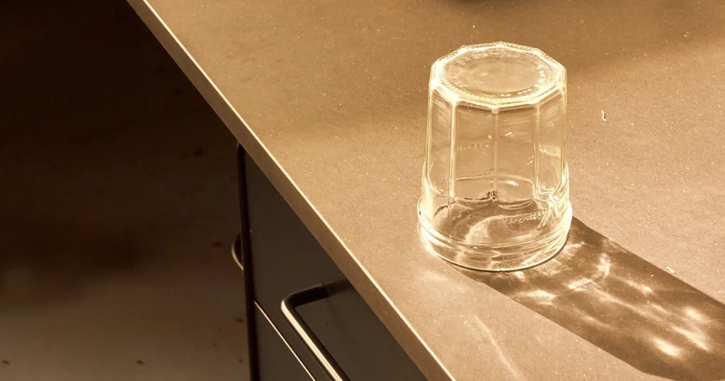Upside-down glass jar on a table casting a long reflection and shadow in warm light.