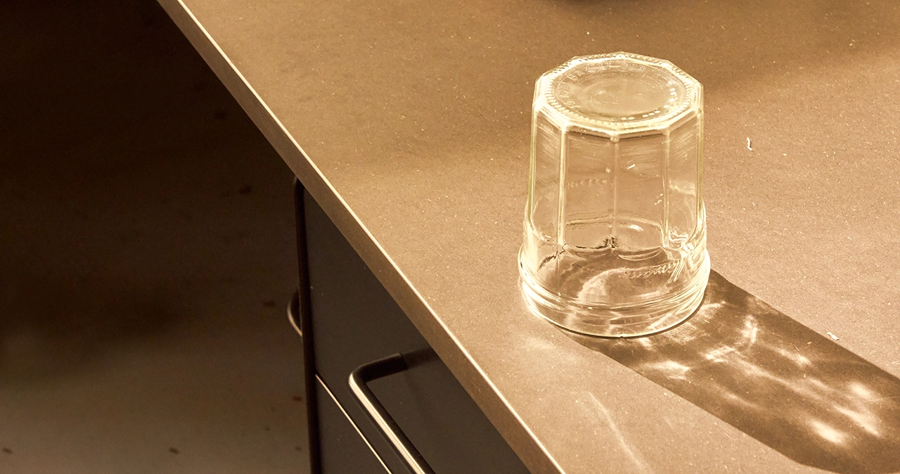 Upside-down glass jar on a table casting a long reflection and shadow in warm light.
