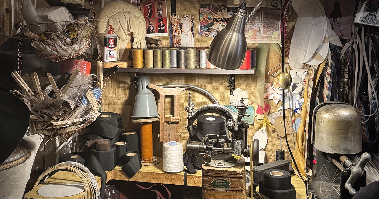 Millinery studio filled with hat-making tools, thread, sewing equipment, and works in progress.