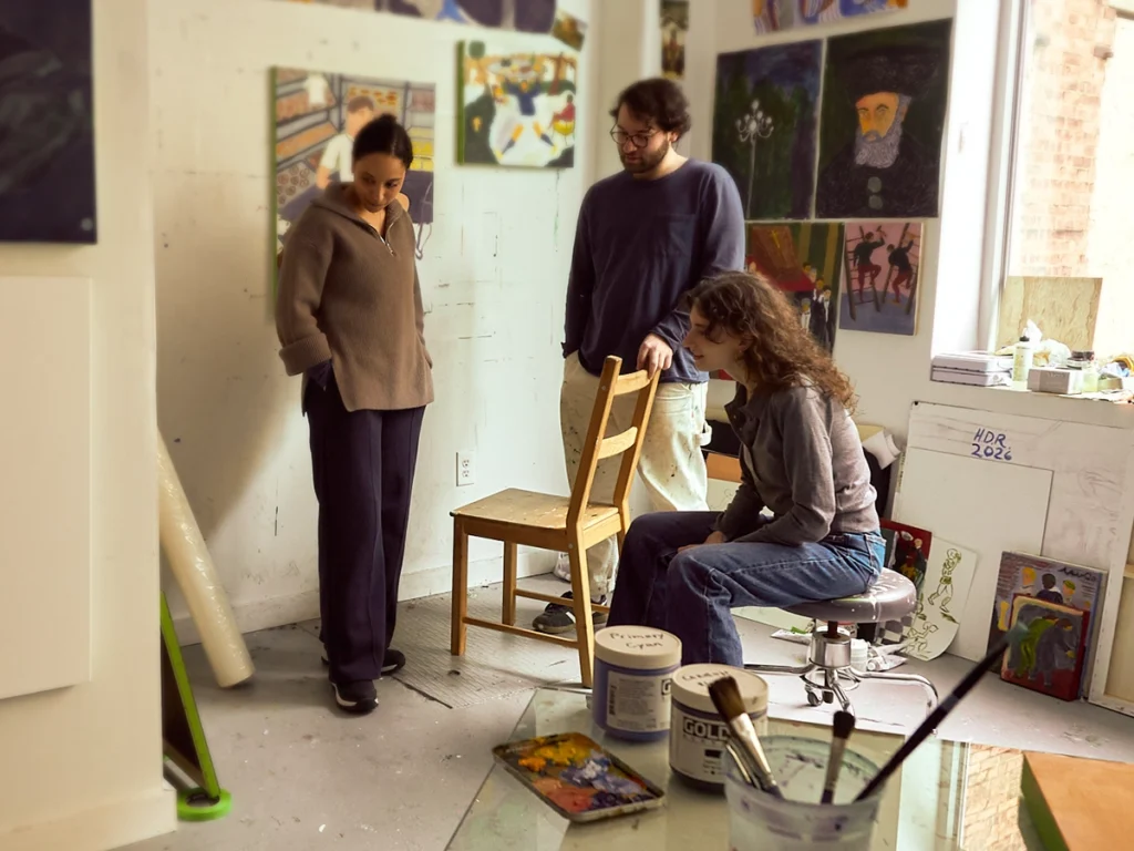 Two women looking at artwork and talking with an artist in his studio