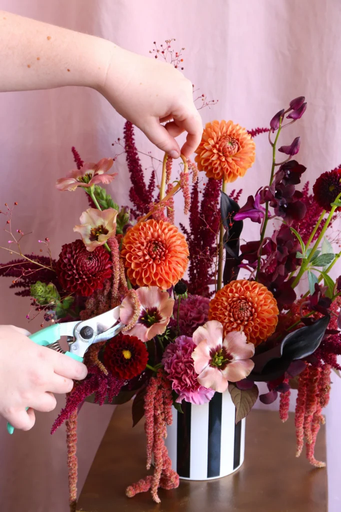 Close-up of a fall floral arrangement with orange dahlias, burgundy flowers, pink blooms, and textured greenery.