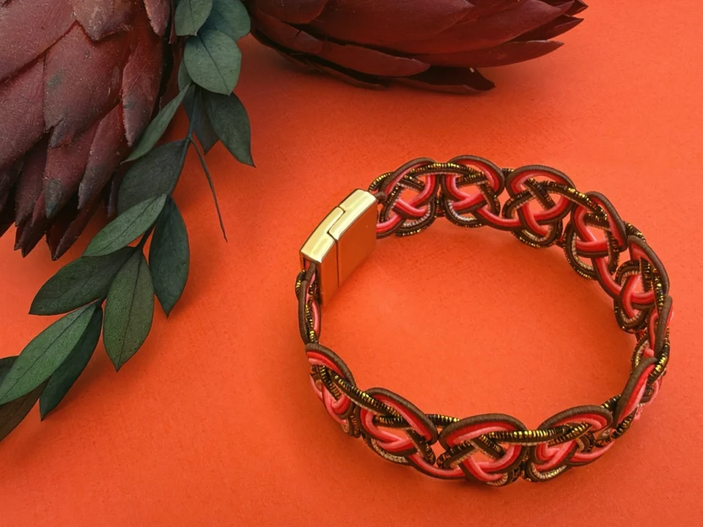 Handwoven mizuhiki bracelet made with coral and bronze washi paper cords using traditional Japanese decorative knotting techniques.