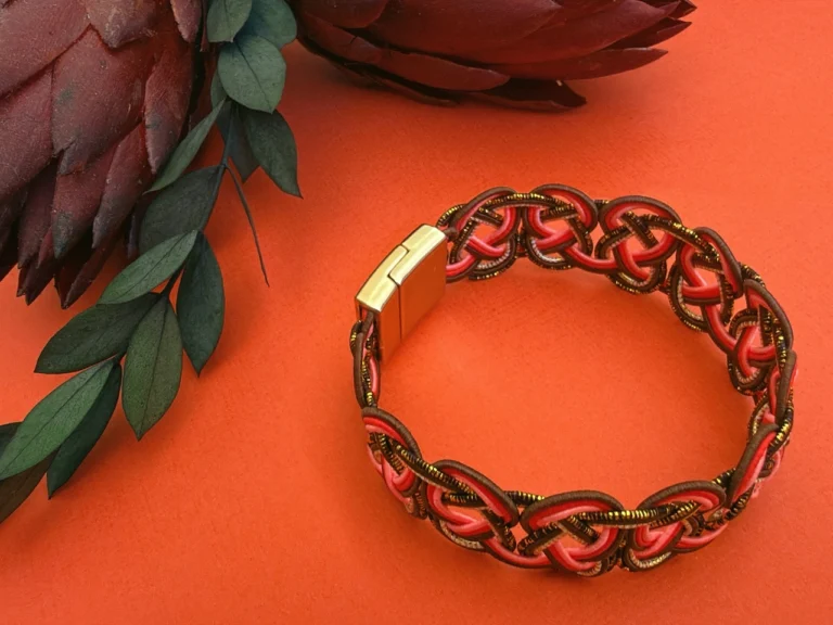 Handwoven mizuhiki bracelet made with coral and bronze washi paper cords using traditional Japanese decorative knotting techniques.